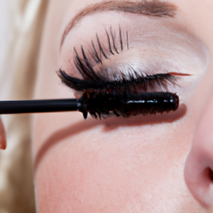 A close-up of a mascara wand being applied to a set of long eyelashes.